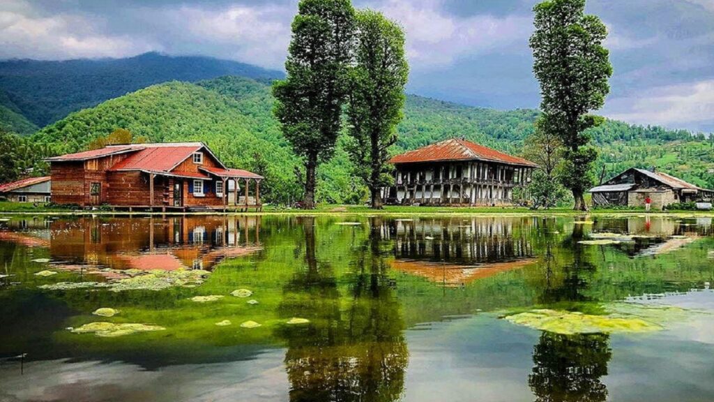 نمای زیبایی از یک خانه چوبی سنتی در کنار یک عمارت قدیمی در کنار برکه‌ای آرام در شمال ایران