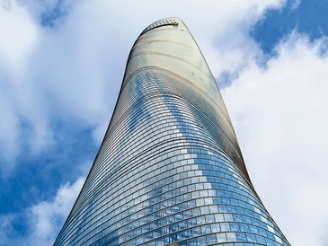 نمای شیبدار و پیچ‌خورده برج شانگهای از پایین به بالا، با جزئیات ساختار شیشه‌ای آن در روز آفتابی