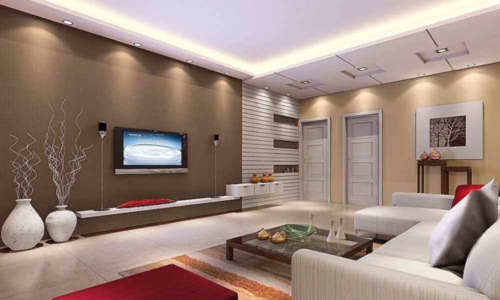 اتاق نشیمن مدرن با دیوارهای قهوهای و کرم، کاناپه سفید الشکل با کوسنهای سفید و قرمز، میز قهوهخوری شیشهای با پایه چوبی تیره، فرش طرحدار با رنگهای گرم