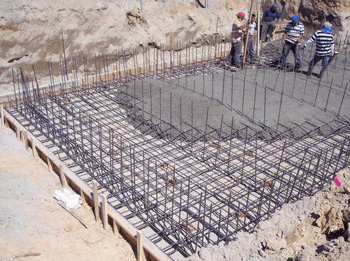 گروهی از کارگران ساختمانی در حال ریختن بتن بر روی شبکهای از میلگردهای فولادی در یک قالب چوبی در یک سایت ساختمانی