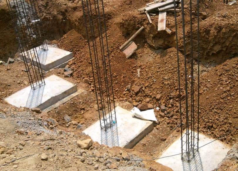 چهار فونداسیون منفرد بتنی مربع شکل با میلگردهای عمودی بیرون زده در یک گودال خاکی