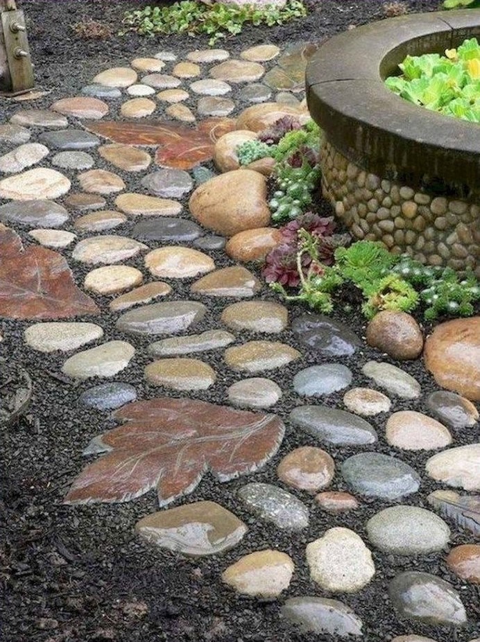 یک مسیر پیادهرو با سنگفرش نامنظم از سنگهای رودخانهای صاف و برگهای سنگی بزرگ در میان خاک تیره، در کنار یک حوض سنگی با گیاهان سبز
