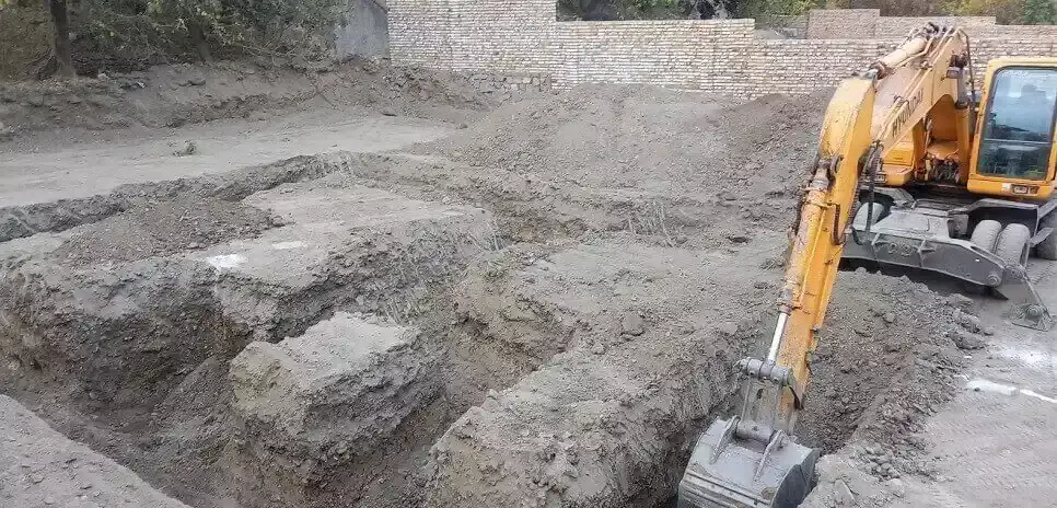 یک بیل مکانیکی زرد در حال حفر یک گودال بزرگ در یک سایت ساختمانی خاکی