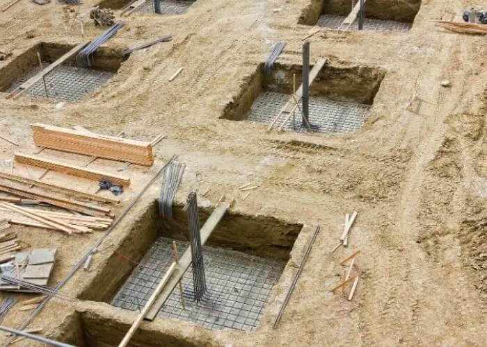 نمایی از بالا از یک سایت ساختمانی در فرانسه با چندین گودال حفر شده که در آنها شبکههای میلگرد برای فونداسیون قرار داده شده و مصالح ساختمانی در اطراف پراکنده است
