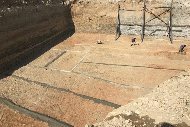 نمایی وسیع از یک گودال بزرگ ساختمانی در فرانسه با چندین کارگر در حال کار بر روی آمادهسازی فونداسیونها در زمین خاکی