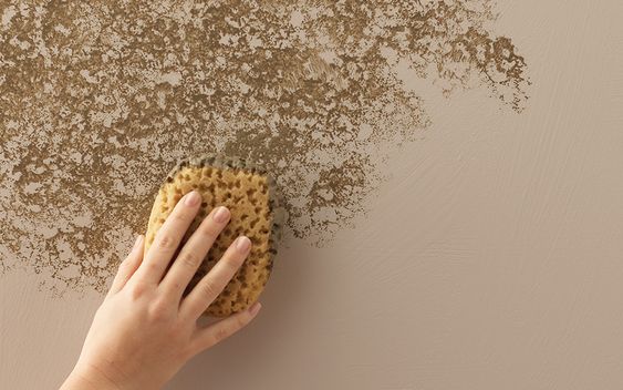 دستی در حال پتینه کاری دیوار با استفاده از اسفنج، ایجاد بافت نامنظم و برجسته