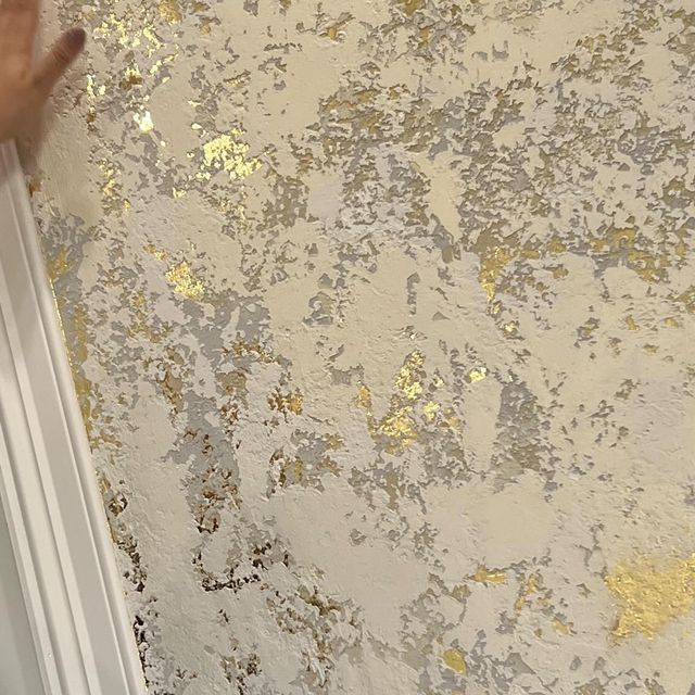 یک نمای نزدیک از دیوار با پتینه کاری برجسته به رنگ‌های کرم، خاکستری روشن و تکه‌های ورق طلای براق