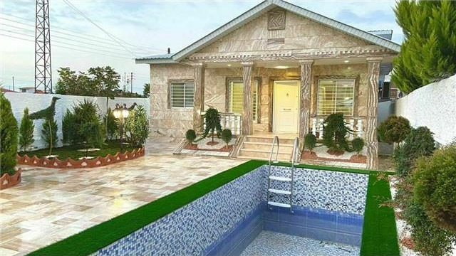 ویلای کلاسیک با نمای سنگی و ستونها، سقف شیبدار، استخر کوچک با کاشی آبی، و محوطه حیاط سنگفرش شده و چمن مصنوعی