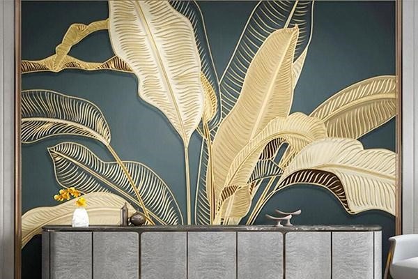 پوشش دیواری سهبُعدی (3D Mural) یا پنل دیواری با طرح برگهای پهن گیاهی به رنگ طلایی روی زمینهی سبز تیره (Teal) یا سرمهای، بالای یک کنسول مدرن سنگی