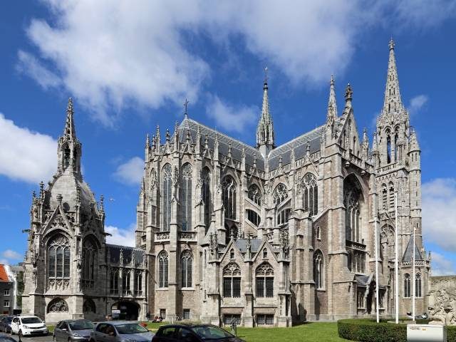 تصویری از نمای خارجی یک کلیسای بزرگ سنگی، احتمالاً کلیسای جامع کانتربری (Canterbury Cathedral) در انگلستان یا کلیسای سنت رومبولد (St. Rumbold's) در بلژیک، که دارای ویژگیهای بارز معماری گوتیک است