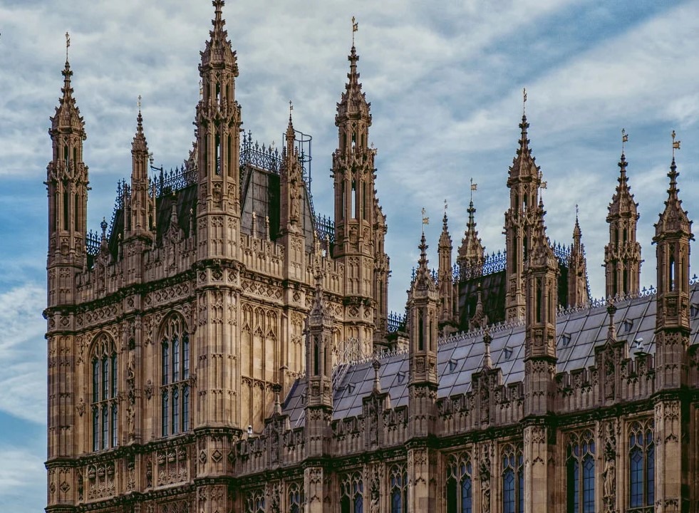 جزئیات نمای بیرونی ساختمان به سبک نئوگوتیک، شامل منارهها (Pinnacles)، تزئینات عمودی و پنجرههای نوکتیز در پسزمینه آسمان ابری