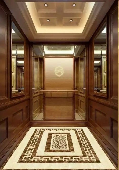 کابین آسانسور کلاسیک با دیوارهای پنل‌بندی شده چوبی قهوه‌ای تیره، سقف کناف نورمخفی، آینه‌های جانبی و کفپوش سنگی با طرح‌های تزئینی و هندسی