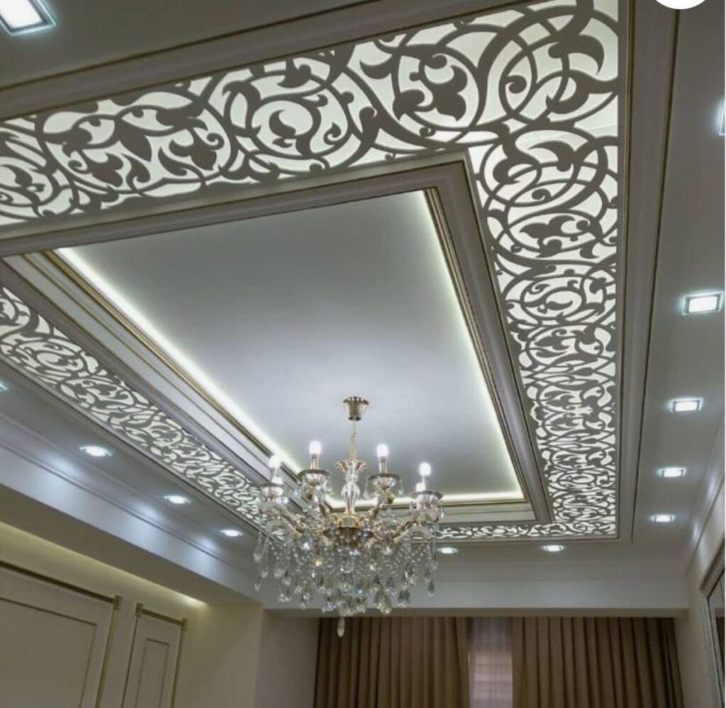 طراحی داخلی سقف پذیرایی کلاسیک با پنل‌های CNC طرح اسلیمی/سنتی، نورپردازی پس‌زمینه و لوستر کریستالی مجلل