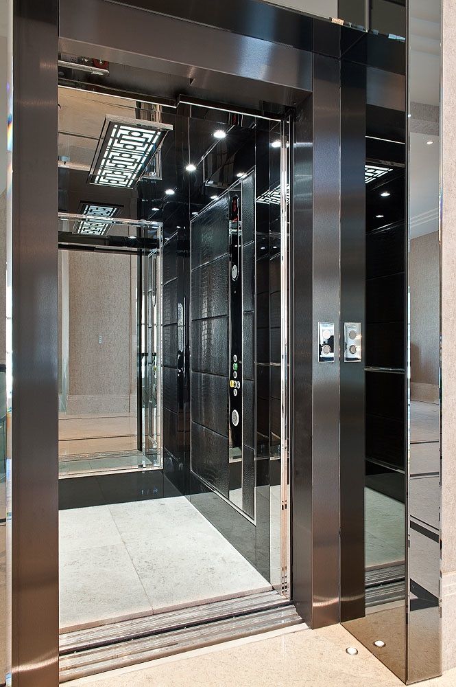 ورودی و کابین آسانسور مدرن لوکس با درب‌های آینه‌ای مشکی و پنل‌های جانبی آینه‌ای، همراه با دیواره کابین بافت‌دار مشکی و سقف نورپردازی شده