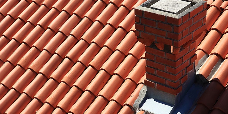 سقف شیبدار پوشیده شده با کاشیهای سفالی (تایل) قرمز و جزئیات فلاشینگ در اطراف دودکش آجری