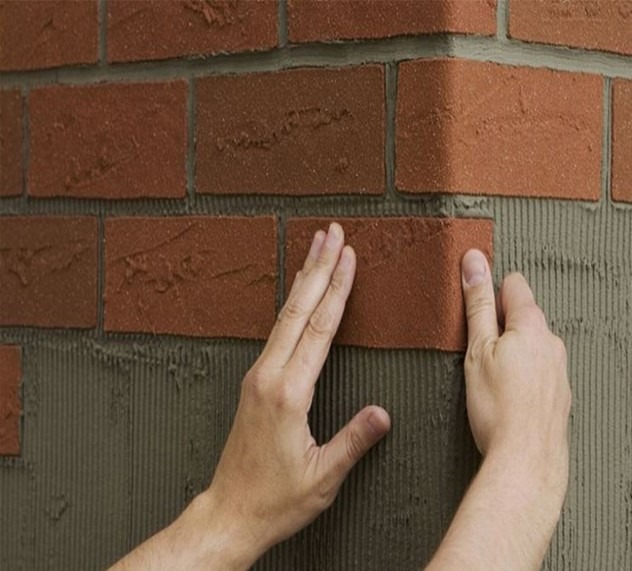 نصب تایل‌های آجری نازک (آجر نما) روی یک سطح عمودی با استفاده از چسب کاشی/ملات سیمانی با دندانه‌کاری، توسط دست کارگر، برای ایجاد نمای آجری سبک