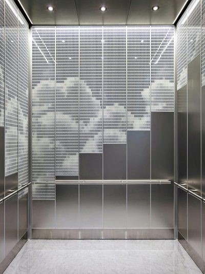 کابین آسانسور فوق مدرن با دیواره پشتی شیشه‌ای/فلزی طرح‌دار (الگوی مشبک سفید)، نورپردازی پشت پنل، دیوارهای استیل خش‌دار و کفپوش سنگی روشن