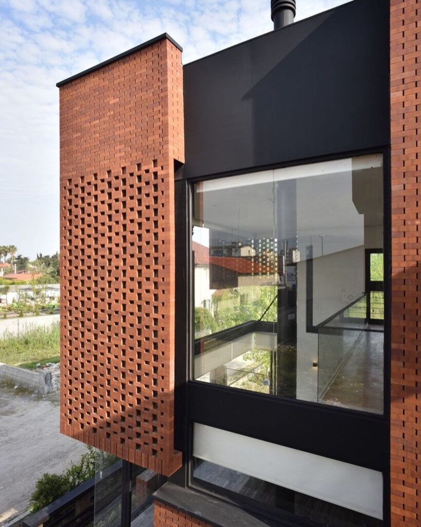 جزئیات نمای یک ساختمان با دیوار آجری مشبک (آجرکاری به صورت سوراخ‌دار و حائل)، ترکیب شده با پنل‌های فلزی تیره و پنجره‌های بزرگ، که به عنوان یک پوسته دوم عمل می‌کند