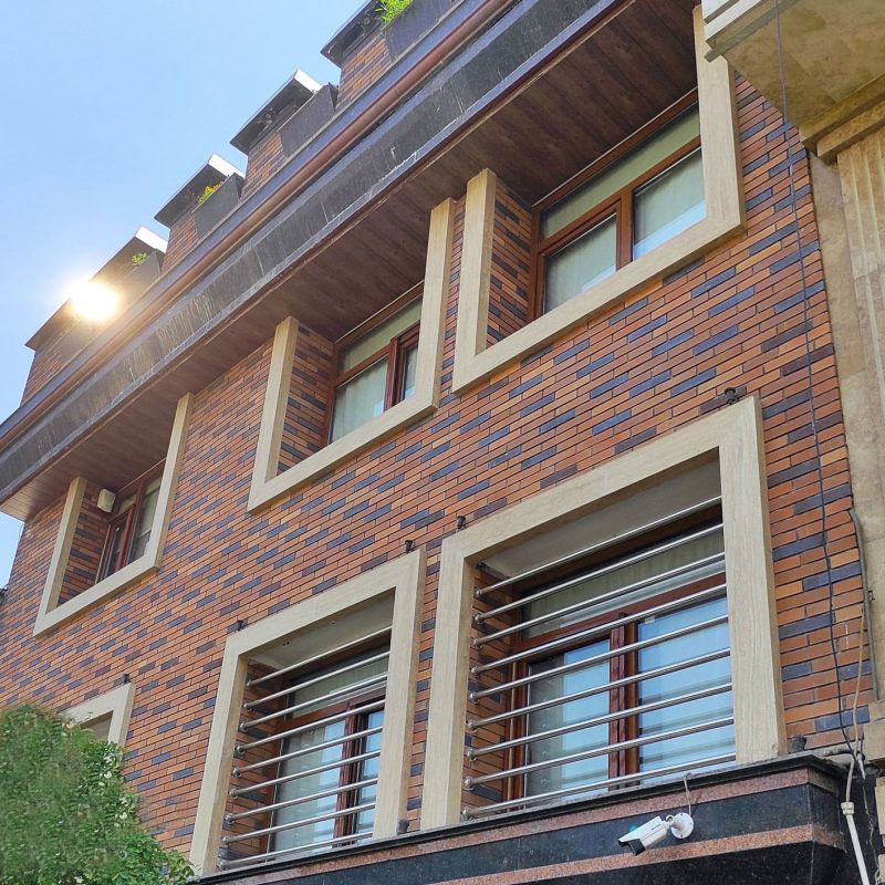 نمای آجری ساختمان تلفیقی با آجر دو رنگ، فریم‌های سنگی برجسته پنجره، و سقف سایه‌بان چوبی، طراحی نمای آجری با حفاظ استیل