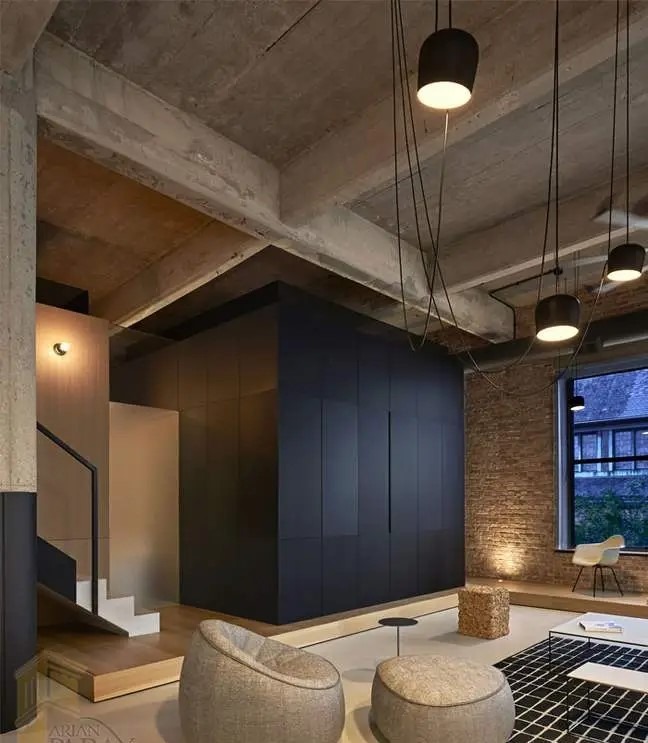 فضای داخلی لوفت با سقف بتنی و تیرهای نمایان، مکعب مرکزی مشکی، پلکان چوبی و نورپردازی آویز مشکی در پذیرایی