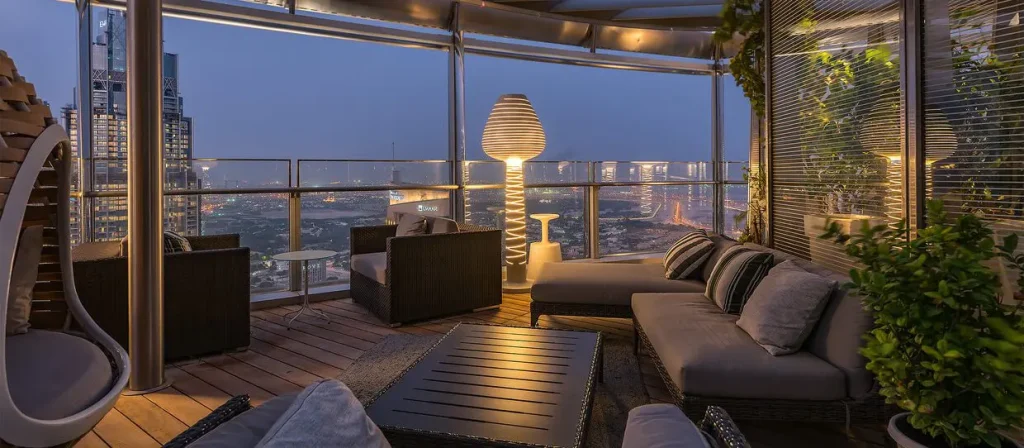 دکوراسیون داخلی تراس پنت‌هاوس لوکس در برج خلیفه دبی در شب، با مبلمان چوبی و مدرن و نمای شهری چراغانی در پس‌زمینه